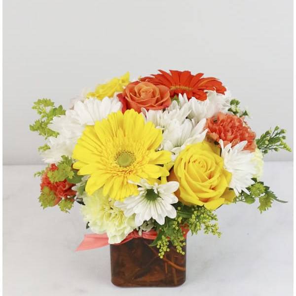 Bright mixed flower arrangement in a square glass vase