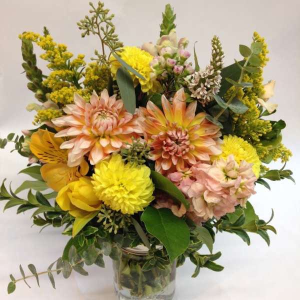 Mixed yellow and peach flowers arranged in a clear glass vase