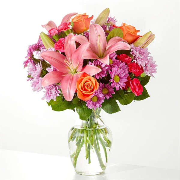 Pink lilies, orange roses, and purple daisies in a clear glass vase