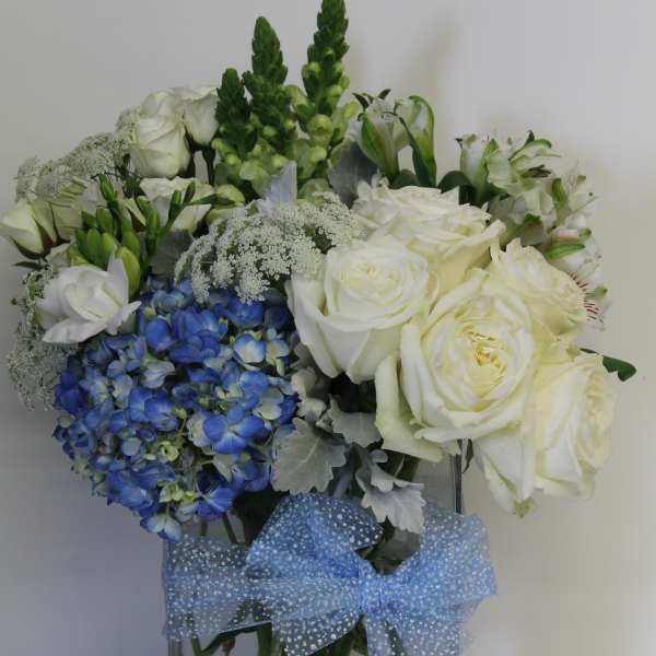 White rose and blue hydrangea arrangement in a clear vase with a blue polka dot bow