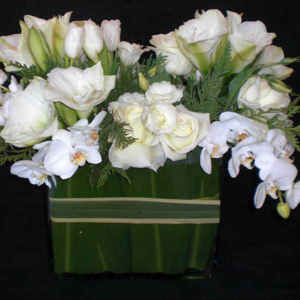 White floral arrangement with orchids and roses in a green vase