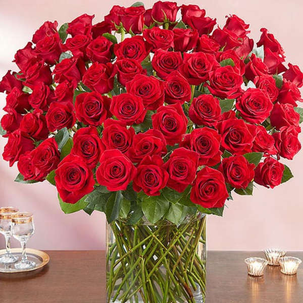 Large bouquet of red roses in a clear glass cylinder vase on a wooden table