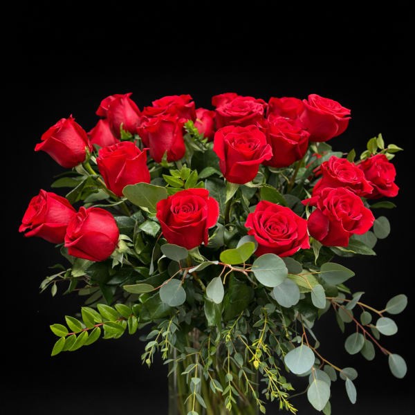 Red roses arranged in a clear glass vase with eucalyptus