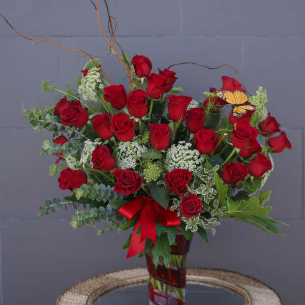 Red roses arranged in a glass vase with a red ribbon and butterfly accent