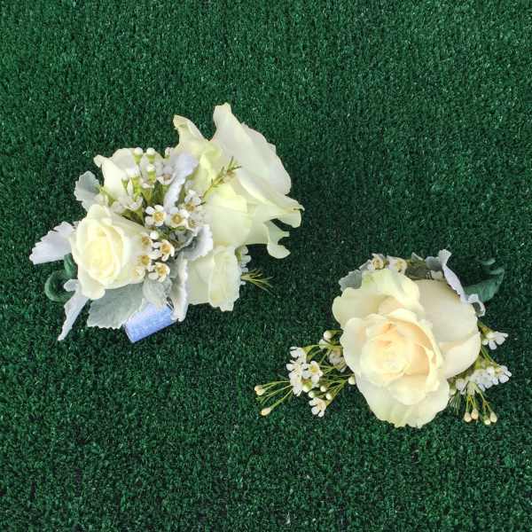 Two ivory rose corsages with small white flowers on green turf