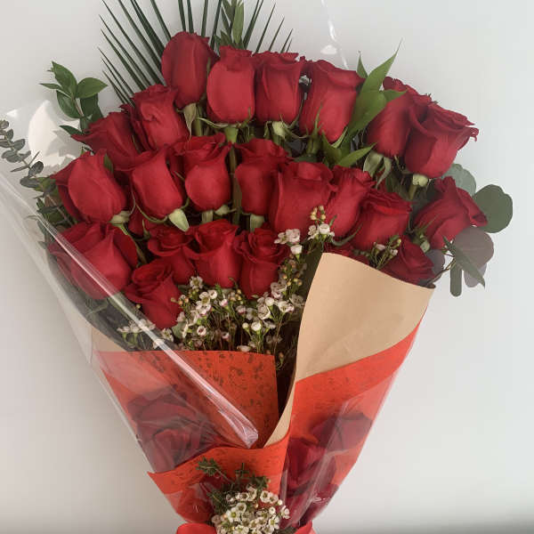 Bouquet of red roses wrapped in red and clear paper with a ribbon