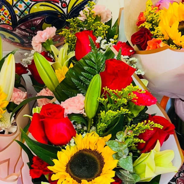 Bouquets of red roses, sunflowers, and lilies wrapped in pastel paper