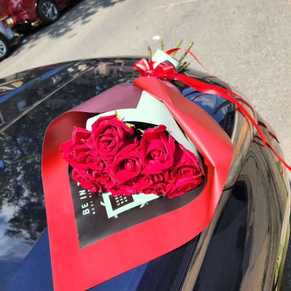 Bouquet of red roses wrapped in red paper on a car hood
