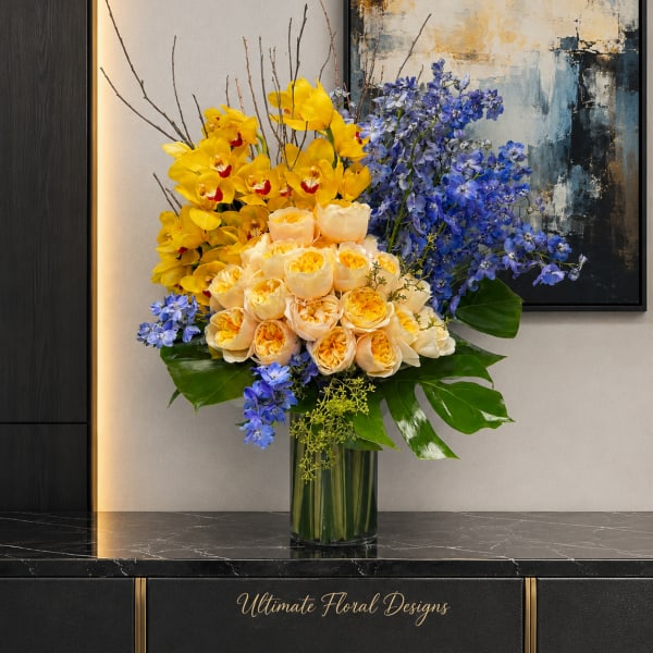Yellow and peach roses with blue flowers in a glass vase