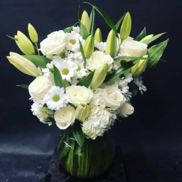White roses and lilies arranged in a green glass vase
