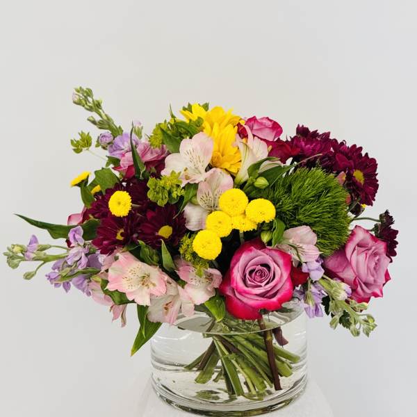 Mixed bouquet of pink, yellow, and purple flowers in a clear glass vase