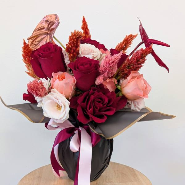 Bouquet of red, pink, and white roses in black wrap with ribbon