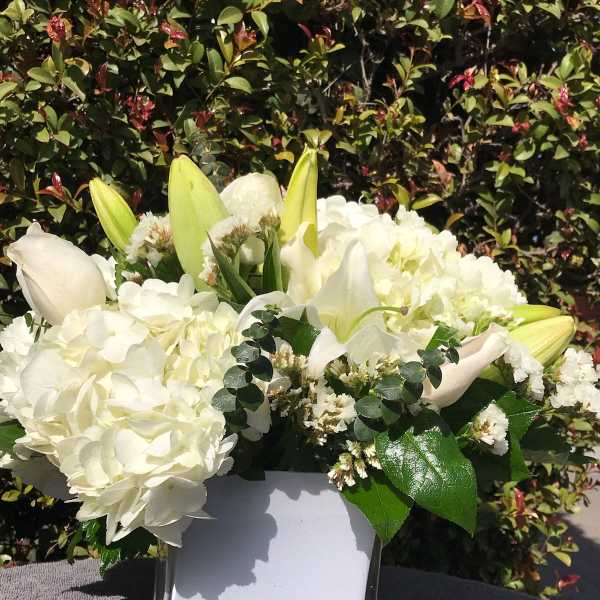 White floral arrangement in a square vase with lilies and hydrangeas