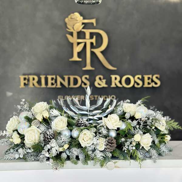White roses arranged with frosted greenery and pinecones in a low centerpiece.