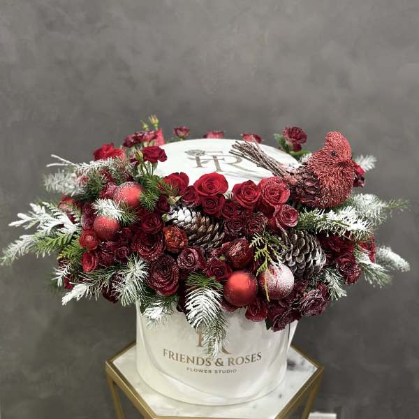 Red rose arrangement in a white hatbox with a decorative bird and pinecones