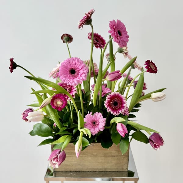 Pink gerbera daisies and tulips arranged in a wooden box