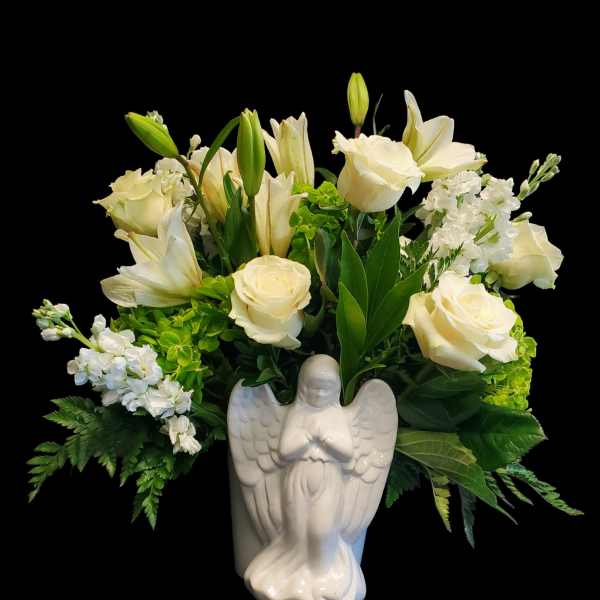 White roses and lilies arranged in a ceramic angel vase