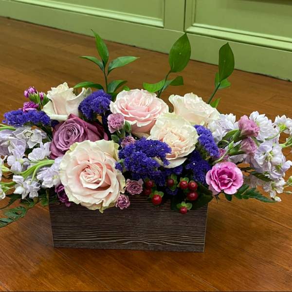 Low floral arrangement with pink, white, and purple blooms in a wooden box