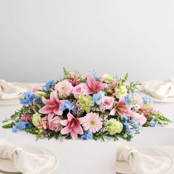 Low floral centerpiece with pink lilies, roses, and blue flowers on a white table