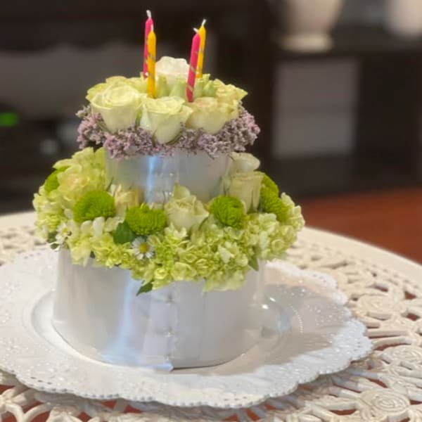 Two-tier floral cake with white roses and green flowers topped by candles