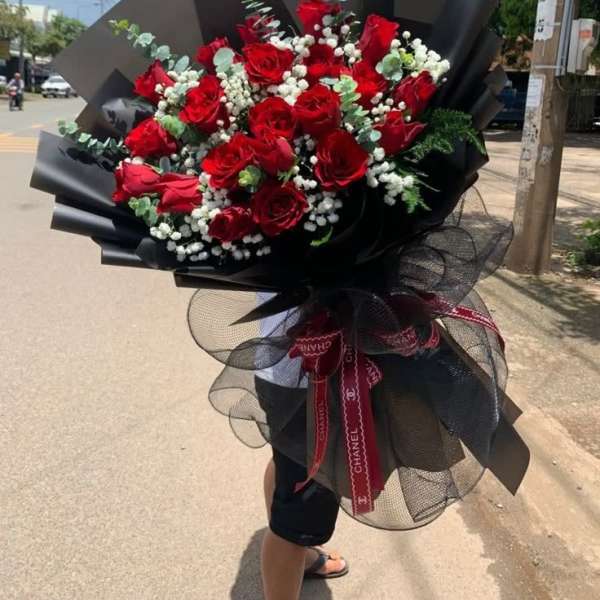 Large bouquet of red roses with white filler flowers wrapped in black paper