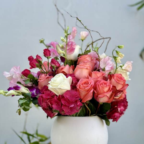 Pink and coral roses arranged in a white vase