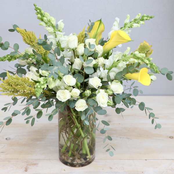 Tall arrangement of white roses, white snapdragons, and yellow calla lilies in a clear glass vase