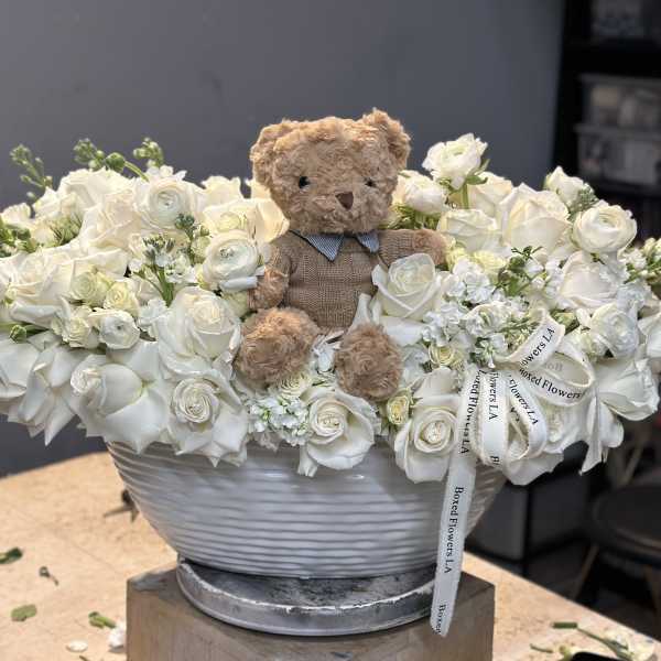 White rose arrangement with a teddy bear in a gray bowl vase