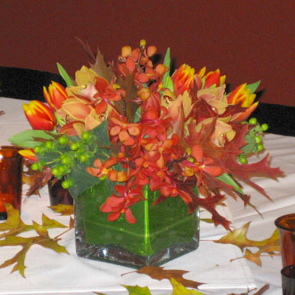 Autumn floral centerpiece in a square glass vase with orange and yellow blooms