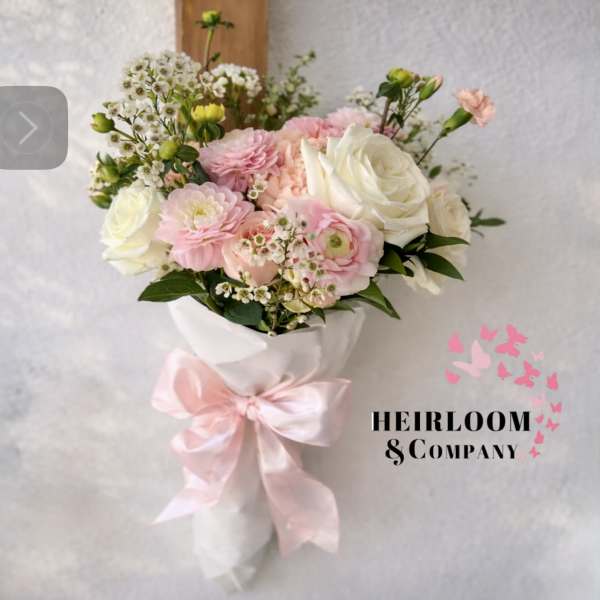 Pink and white bouquet with roses and small filler flowers, wrapped in white paper with a pink ribbon