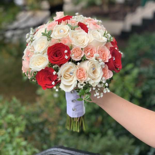 Handheld bouquet of red, white, and blush roses with baby's breath