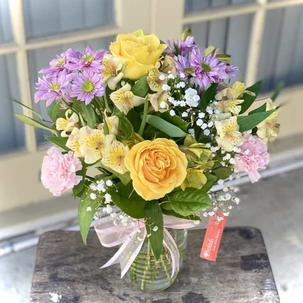 Bouquet of yellow roses, purple daisies, and pink carnations in a glass vase