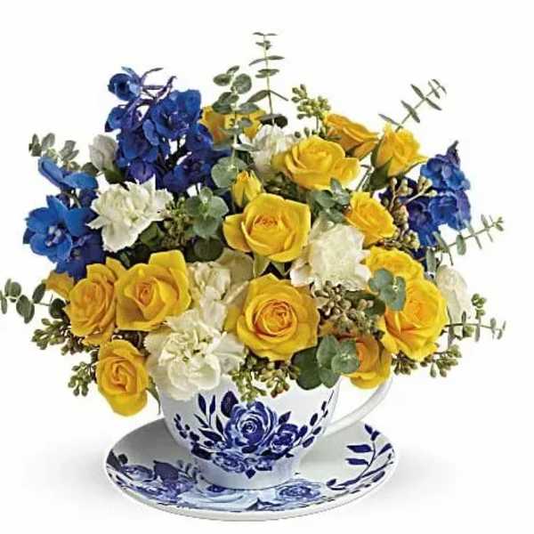 Yellow and blue roses arranged in a teacup with matching saucer