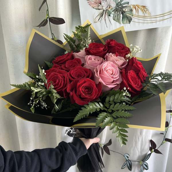 Bouquet of red and pink roses wrapped in black paper with gold trim