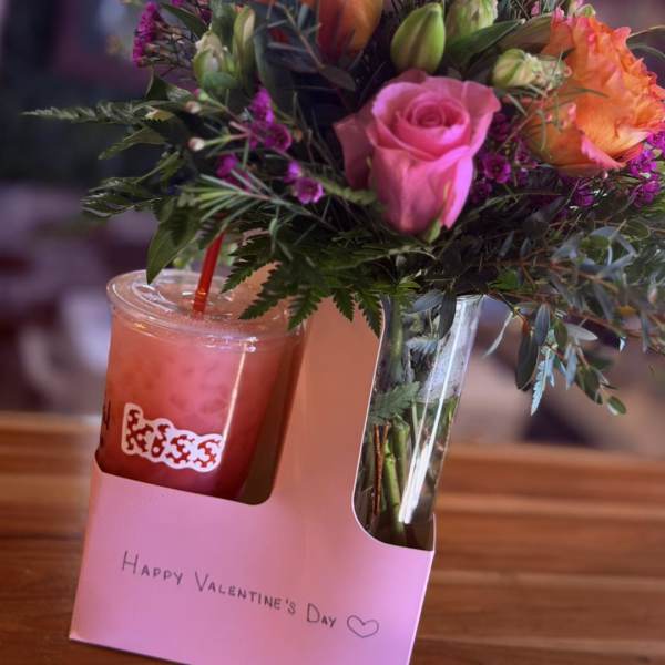 Pink and orange roses in a clear vase beside a pink drink cup.
