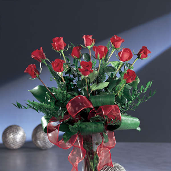 Red roses arranged in a clear glass vase with red ribbon