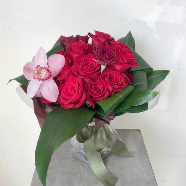 Bouquet of red roses with a pink orchid and broad green leaves