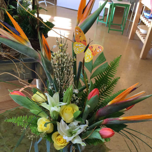 Tropical bouquet with yellow roses, white lilies, and bird-of-paradise flowers in a glass vase