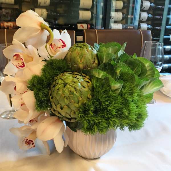 White orchids and green artichokes arranged in a white vase