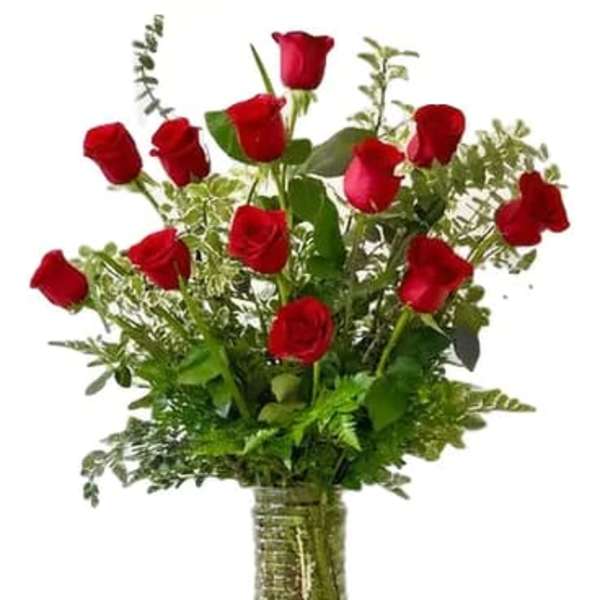 Red roses arranged in a clear glass vase with greenery