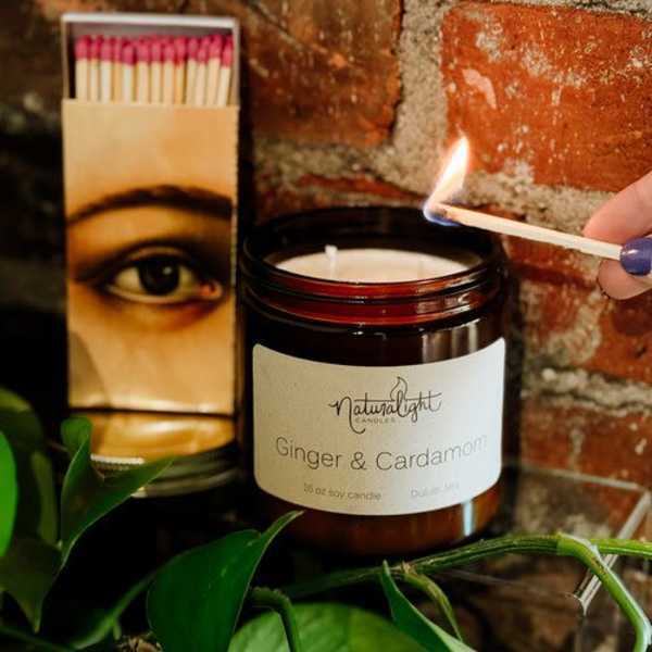 Amber jar ginger and cardamom candle being lit with a match beside a matchbox.