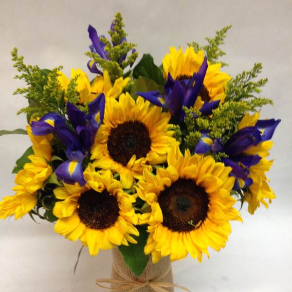 Bouquet of yellow sunflowers and purple irises in a burlap-wrapped vase
