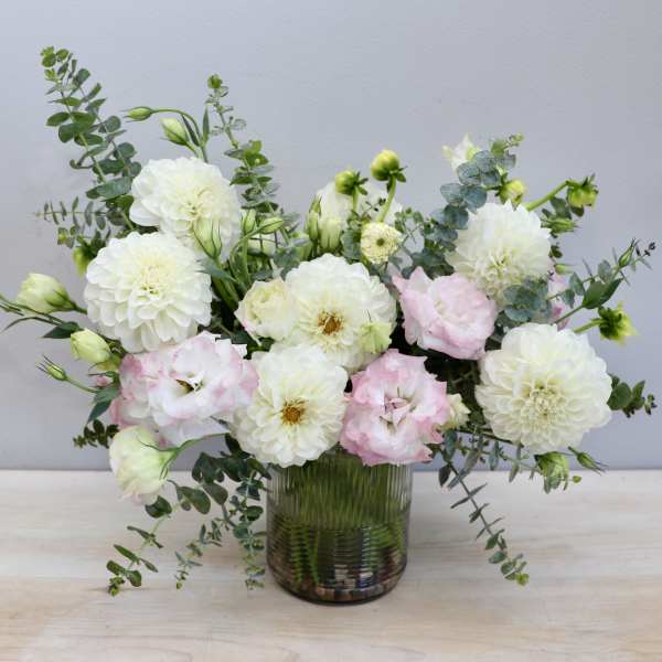 Low glass vase of white dahlias and pale pink lisianthus with airy greenery.