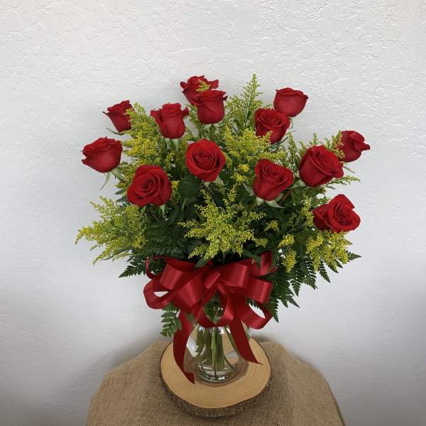 Red roses arranged in a glass vase with a red ribbon