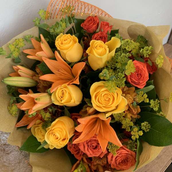 Bouquet of yellow and orange roses with orange lilies wrapped in brown paper