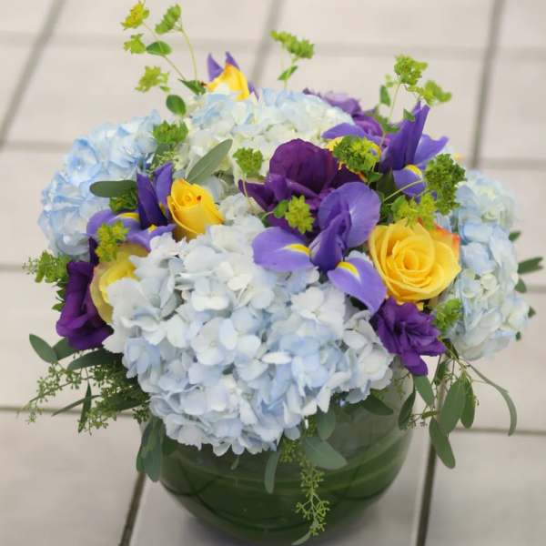 Blue hydrangeas with yellow and purple roses in a green vase