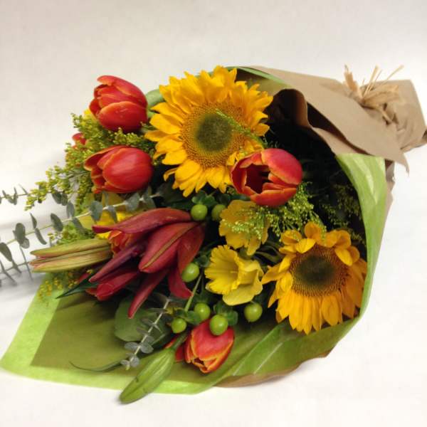 Bouquet of sunflowers, red tulips, and yellow lilies wrapped in paper