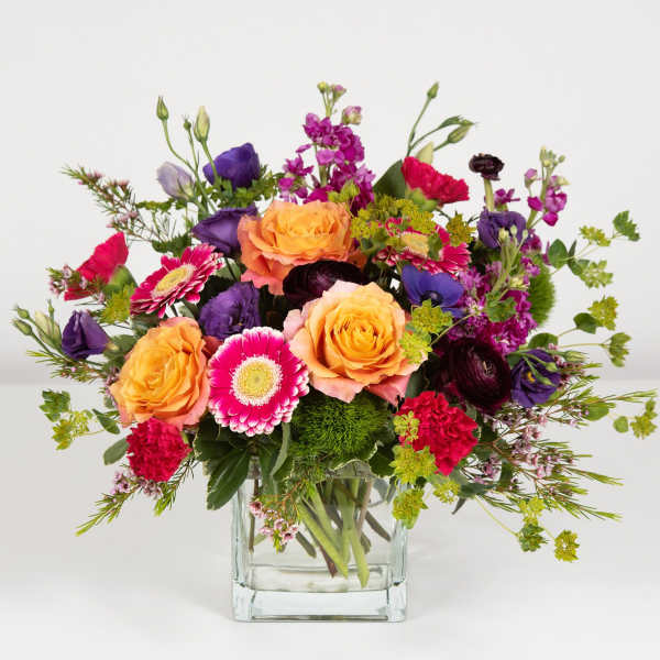 Mixed bouquet of orange, pink, and purple flowers in a clear glass vase