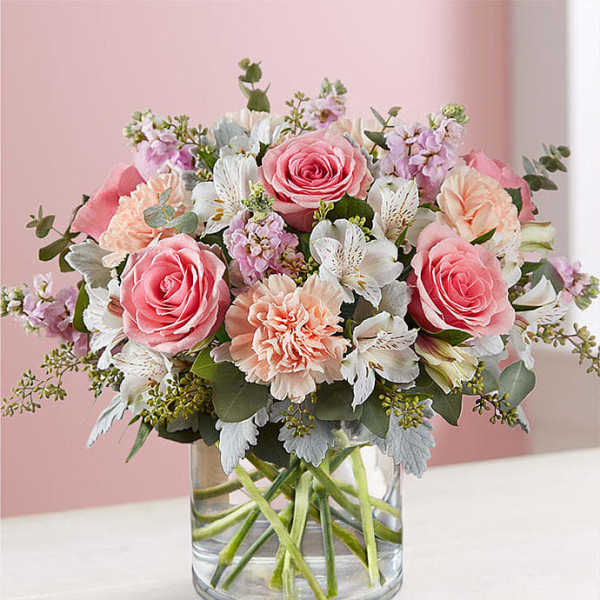 Pink and peach bouquet of roses, carnations, and white alstroemeria in a glass vase
