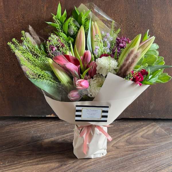 Mixed bouquet of lilies, pink blooms, and white flowers wrapped in paper
